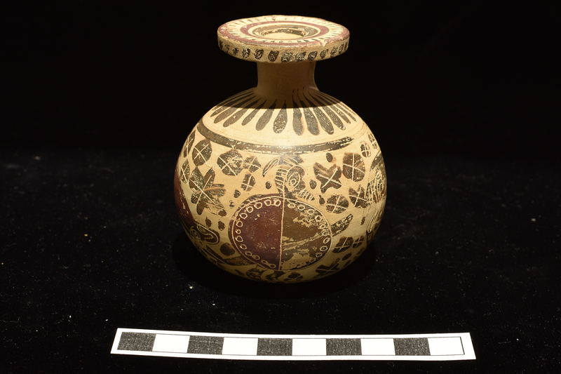 Small full-bodied aryballos.  Main decoration around body between two stripes: warrior opposite handle and two grazing deer around back and sides, blob rosettes in field; figures decorated with incision and added red, rosettes with incision only.  Base decorated with stripes radiating from central annulus.  Radiating elongated drops on shoulder; irregular dots on edge of rim, surface of rim decorated with 3 concentric stripes with elongated triangles radiating inward from exterior stripe; two broad stripes on exterior handle.