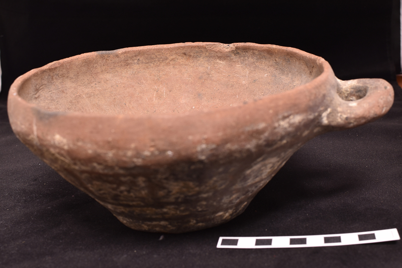 Flat-bottomed bowl with inturned rim and incrusted decoration on exterior.  Primary decoration consists of two broad stripes around lower body above which a row of approximately solidly painted squares and at juncture of body and rim stripe with pendant loops; traces of now largely fugitive X’s in each square.  Traces of stripe on roughly horizontal loop handle of circular section attached just below rim.
