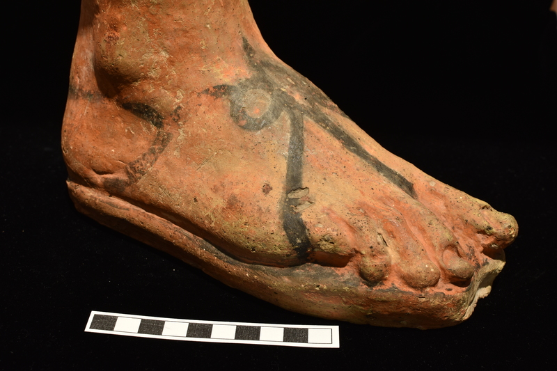 Right foot, hollow but with solid sole plate with vent hole at heel; top surface about flat with central hole.  Toes articulated, but poorly shaped with no appreciable articulation of joints; toenails sharply articulated on big toe and first toe, faint to no articulation on remaining toes.  Ankle bones articulated inside and out.  Resting on thick base.  Coated all over except for broad strip on inside of ankle and under side of base with red paint and sandal painted in black: represented as thin sole, from which rise at heel thin straps which tie in bow at top of foot & from which extend 3 straps, 2 reaching to sole at sides, 1 reaching to sole between big and first toe; single strap around heel.