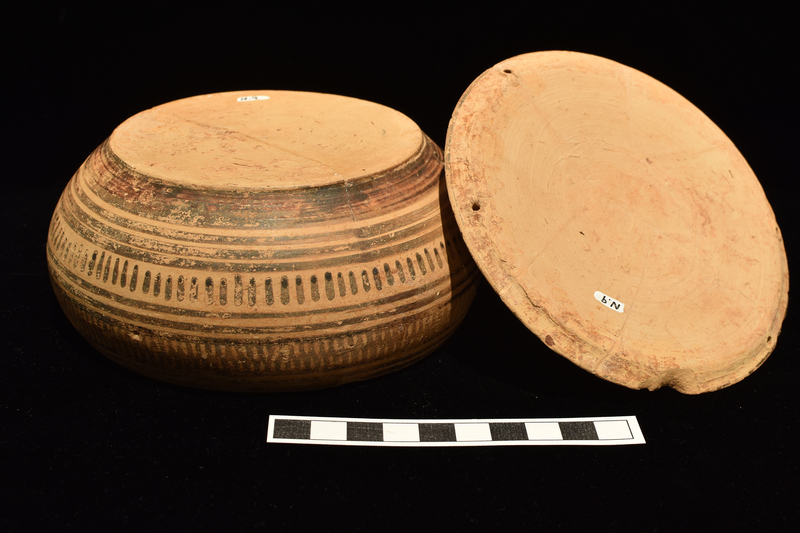 N.9a: Low shallowly convex body decorated, between bands of groups of 3 narrow stripes, w upper zone of multiple zig-zags, lower zone of short vertical stripes;  broad stripe at base.  Two pairs of suspension holes opposite one another on inner rim. N.9b: Fairly flat lid with tall conical handle; concentric stripes around surface of lid, narrow at edge; single broad stripe at center; and solidly coated at base of handle which is decorated with concentric narrow stripes.  2 pairs of suspension holes opposite one another near edge.