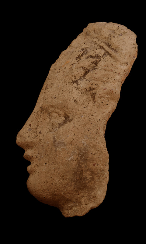 Head with melon hair-do rising from forehead to fillet tied in Hercules-knot with horizontal braid above.  Brows, lids, and pupils articulated; prominent nose above poorly fashioned open lips; fairly broad surfaces of cheeks, prominent rounded chin.  Traces of white slip all over, traces of black paint on hair.