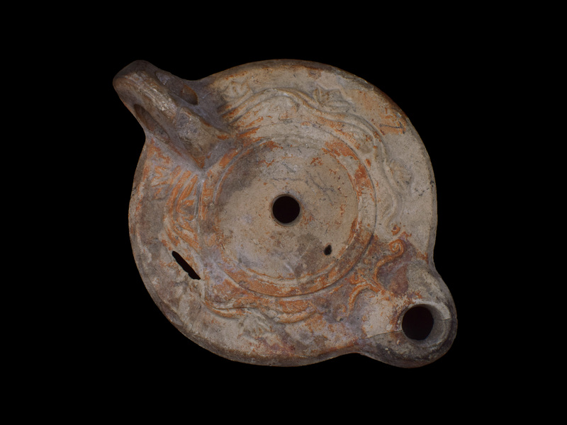 Low, sharply carinated reservoir on flat base defined by incised line; within which across center impressed CIV(LIUS) PHIL(IPPUS); horizontally pierced vertical loop handle from shoulder to base w two incised lines on top surface spreading to plain, concave discus which  defined by low raised border; small air hole behind short  round nozzle.  On  shoulder stylized vine  in relief w volute device on base of nozzle.  Coated w red paint.  Some darkening of nozzle.
