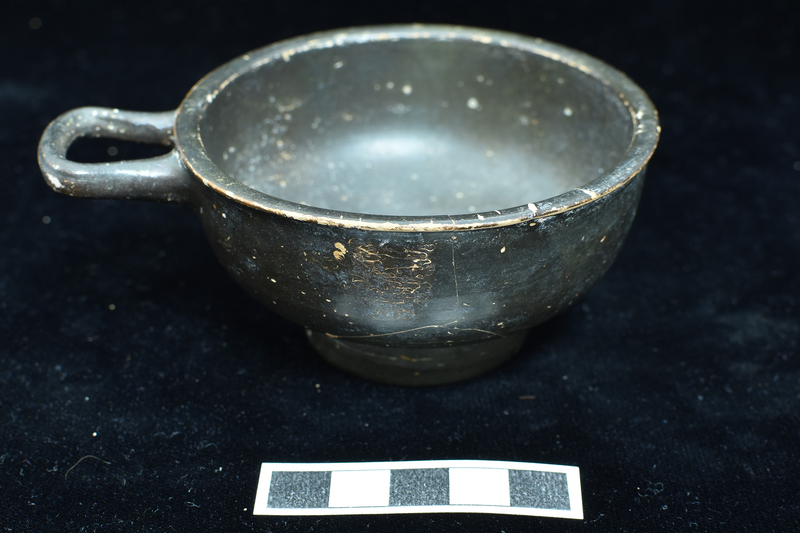 One-handled cup w raised base and single horizontal handle, slightly projecting lip.  Solidly coated