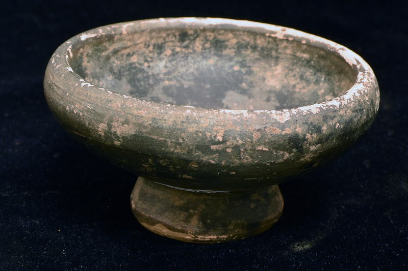 Bowl w convex sides rising fr pedestal base, nippled convex conical underside, to rounded shoulder & thick plain rim. Coated all over int and ext body and most of ext base w dark paint which splashed onto edge of underside of base.