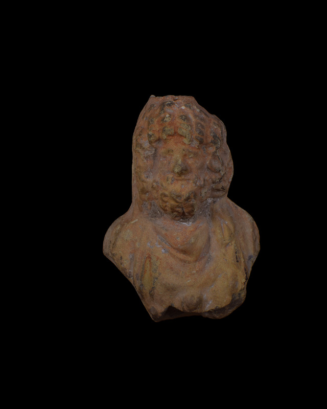 Mouldmade finial, w bust of Zeus apparently rising from floral element visible at back as large leaf which at sides finished as shallowly concave surfaces on side of bust.  Head of Zeus surrounded by curly hair & beard w eyes under prominent brows, nose & mouth articulated; at back, merges into back of second smaller head w long hair bound by fillet, crown strands & curls indicated by incision (?Ganymede).  Zeus in chiton  which falls in front in V-shaped folds, vertical from r shoulder, w swath of himation coming from rear over l shoulder; ?floral element in center of chest.  Completely coated in red paint.