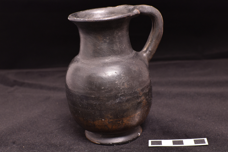 Jug with shallowly concave cylindrical neck with outturned rim, high offset base; double handle from shoulder to rim where attachment of coils extended into flange-like projections on either side.  Burnished on ext and int rim.