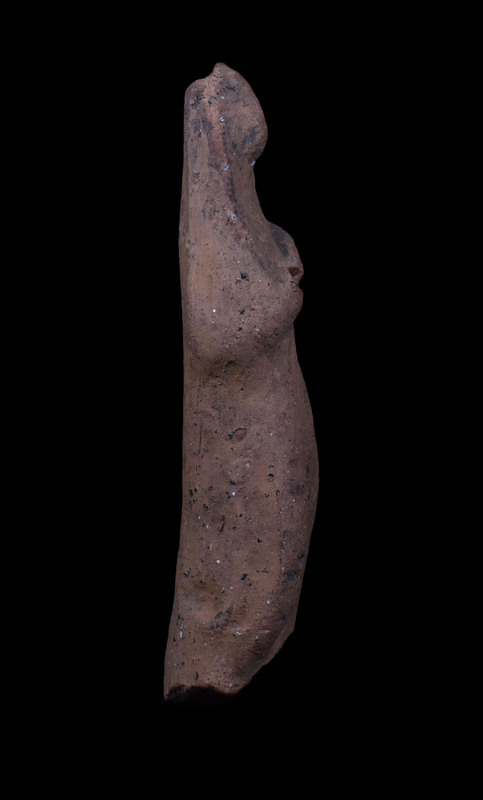 Mouldmade standing figure w palla draped over head and falling on either side, pulled across body diagonally over r arm; l arm at side holding vertical clump of drapery; slightly projecting right knee.  Pinched ridge of clay articulating face.  2 large vent holes in back.