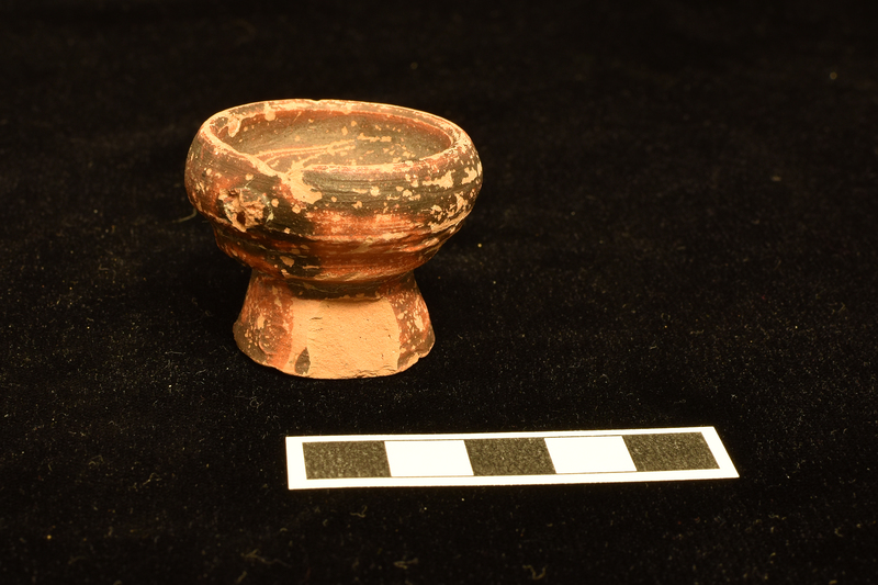 Bowl with tall inturned rim on high truncated conical pedestal foot; prominent horizontal ridges on lower bowl, giving impression of wheel marks; definite wheel marks on sides and underside of base.  Bowl inside and out solidly coated with splash of paint on underside of base.