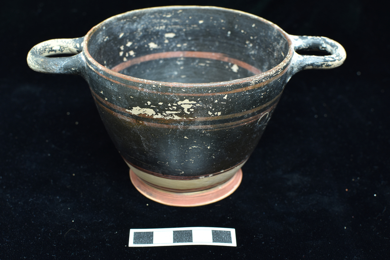 Partially coated skyphos w stripes in added red.  Interior  & upper 3/4 of exterior coated; stripes in added red around top of rim on ext, two added red  bands below handles, two bands in added red at base of solidly coated portion of ext; just above base two band, lower black, upper red shading to black; base edge int & ext coated red; two concentric dark rings and center dot on underside of base.  Inside bowl one red stripe a mid-H, another at juncture of body & base.