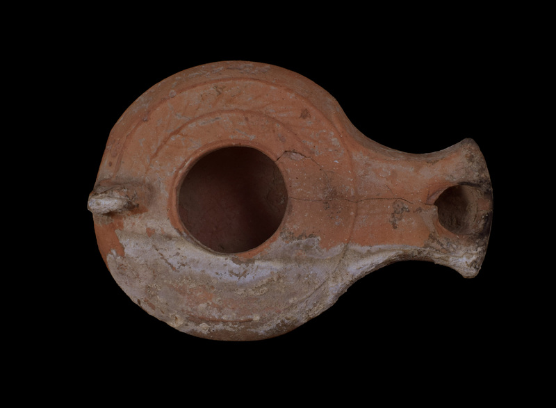 Carinated reservoir w flat discus decorated with stylized palm-branch design in very low relief; small, incomplete horizontal perforation in vertical loop handle attached to top of reservoir, broad spathate nozzle; raised bands articulate edges of underside of nozzle & edge of almost flat base.  Darkening on nozzle.