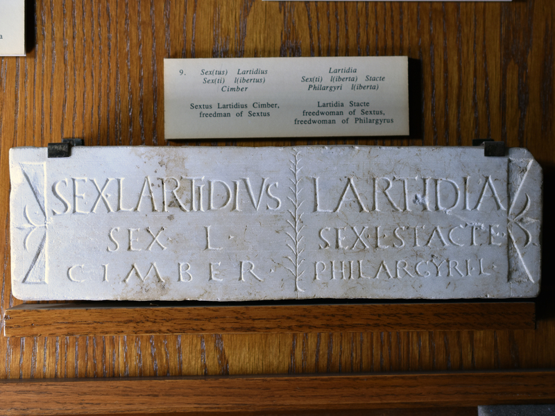 Plain plaque of white marble with decorated left & right margins; the 2 sets of inscriptions separated by a branch.