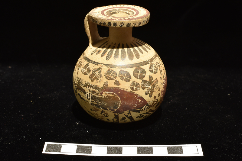 Small full-bodied aryballos.  Main decoration around body between two stripes: warrior opposite handle and two grazing deer around back and sides, blob rosettes in field; figures decorated with incision and added red, rosettes with incision only.  Base decorated with stripes radiating from central annulus.  Radiating elongated drops on shoulder; irregular dots on edge of rim, surface of rim decorated with 3 concentric stripes with elongated triangles radiating inward from exterior stripe; two broad stripes on exterior handle.