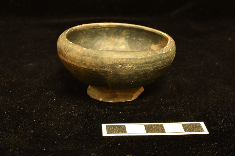 Bowl  with low, but strongly incurved rim on low pedestal base.  Coated inside and out except for underside of base which has some splashes of paint.