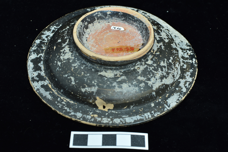 Small  plate  w ring base decorated w impressed decoration on rim.  Shallowly concave bowl w ca h rim decorated with palmettes between 2 incised bands and circle of palmettes around bowl center; offset vertical base with central torus.   Solidly coated except for edge and interior of base.