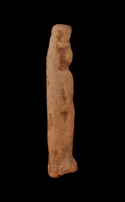 Mouldmade standing female of Dadaelic type with tall polos. Bilaterally symmetrical with arms close to sides, probably wearing simple tunic belted at waist. Triangular contour of face, nose articulated with slight depressions for eyes on either side; some indication of mass of hair straight across forehead. Stands on squarish base, articulated primarily at front.