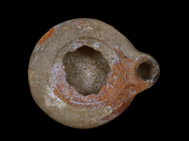 Handleless, low convex reservoir w sharp articulation w broad rim which decorated w row of relief annuli within each of  which relief dot and separated from concave discus by relief band; traces of relief figure in discus; short rounded nozzle at base of which on rim 3 relief dots.  Irregularly flat base defined by 2 concentric incised lines.  Coated all over w red paint; darkened nozzle.