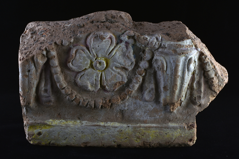 Thick heavy fragment with deep depression at back from which back wall curves up towards edge which is broken off in top three quarters but has finished edges at bottom and toward front surface.  Relief decoration on front: