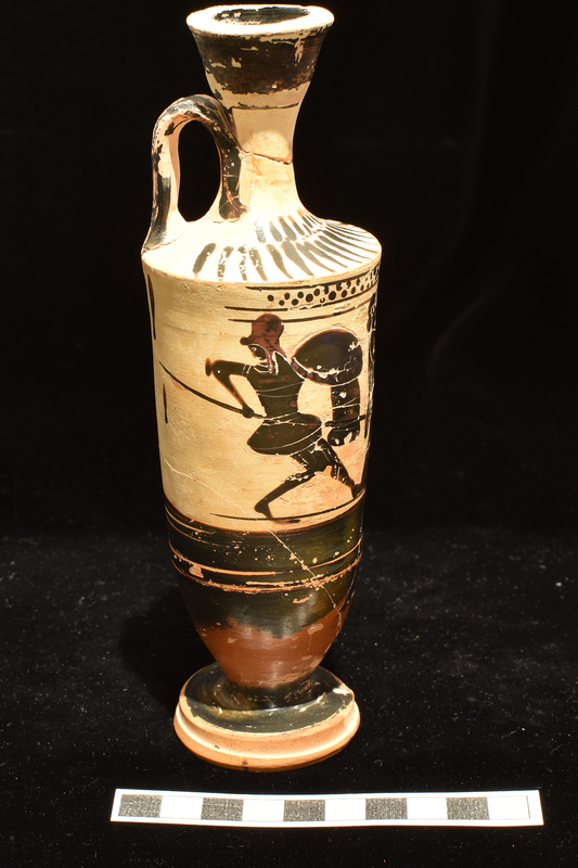 Trumpet-mouthed lekythos w body opposite handle decorated w flute player, facing r, at altar flanked by 2 dancing warriors; decoration in incision & added red; below main zone broad stripe flanked by two narrower stripes, lower body solidly coated to edge of base, exterior of which reserved; above main zone narrow band of dots with one stripe above, 2 below; shoulder decorated w two rows of radiating stripes lower longer than upper w band of dots between; exterior of handle and exterior and interior of mouth solidly coated.