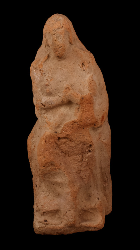 Mouldmade figure seated on low-sided throne, holding infant on left side with r arm across body w hand holding breast to child.  Mass of hair surrounding face, w two clumps over ears; traces of shallow incisions for eyes.  R leg bent back w foot projecting forward diagonally; left foot resting on lower step of two-stepped front of throne.  Vertical paring of back after removal from mould.