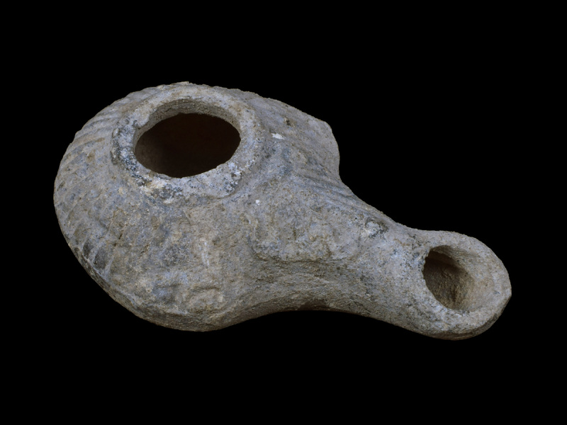 Handleless, carinated reservoir on low raised base; large fill hole w torus moulding border from which lines radiate out to carination; large palmette from torus over nozzle surface; incipient lugs, with relief ?eyes at carination on either side of base of nozzle.  Probably originally painted all over ext.