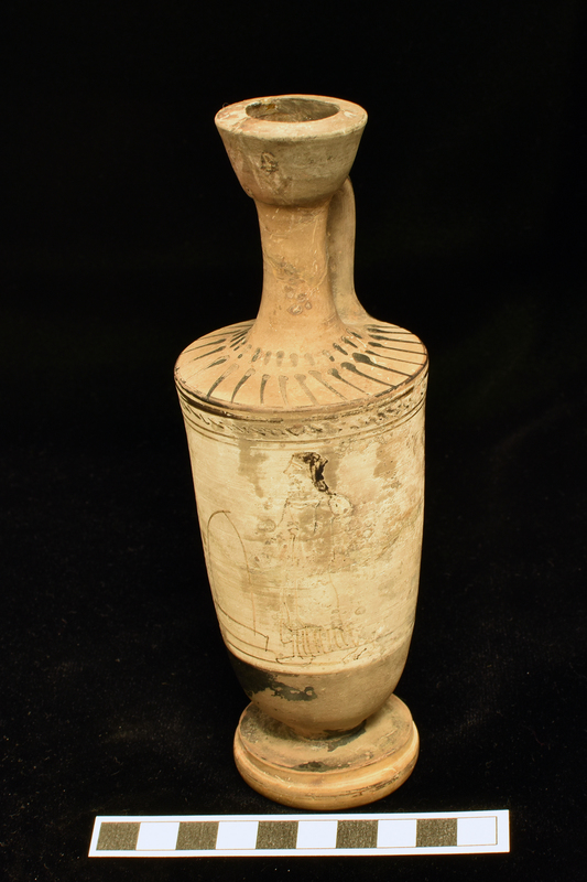 Trumpet-mouth  lekythos with in main white slipped zone opposite handle, badly drawn in dilute glaze, woman in chiton and himation standing before tomb with: 2 stripes below and above 2 stripes and narrow band with irregular diagonal stripes from one side of vase to other above figure d zone.  Lower body, top of base solidly coated, single stripe around top of lower torus of profiled base.  Shoulder decorated with radiating stripes below short band of stripes at base of neck; interior and exterior of mouth and exterior of handle solidly coated.