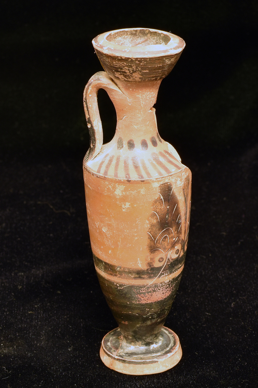Trumpet-mouthed lekythos w int mouth totally coated, ext mouth coated except on int edge of lip; at base of neck row of blobs, v stripes on shoulder; lower body & top surface of foot solidly coated; upper half of body decorated opposite handle w three upright palmettes w rudimentary incision separated by two vertical leaves, each palmette resting on pair of owl-eye-like elements representing volutes; below palmettes broad horizontal stripe and narrow reserved stripe. Band handle coated on ext fr edge of shoulder to top of neck.