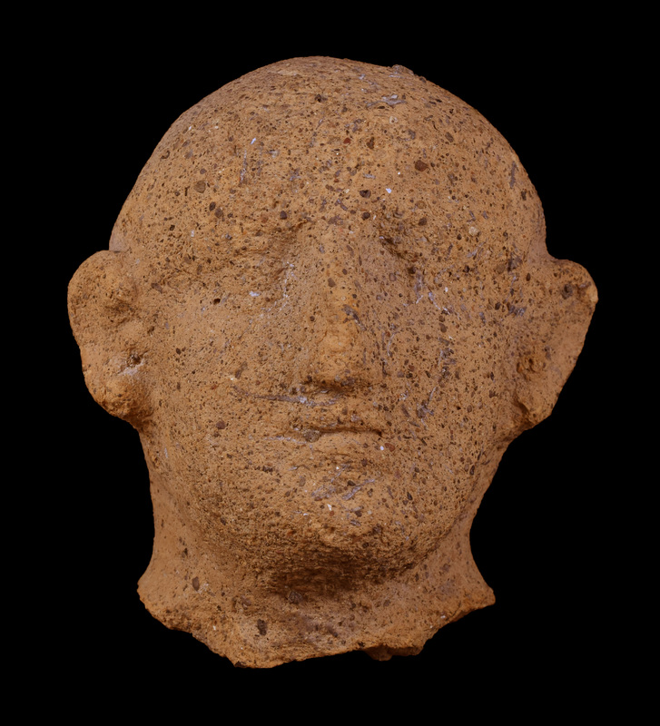 Head of very sandy clay loaded with dark grits, with cap of hair articulated only above very prominent ears and only slight articulation of inner detail; eyes under slightly projecting brows lightly rimmed above and below, strong nose and chin, prominent line between lips.