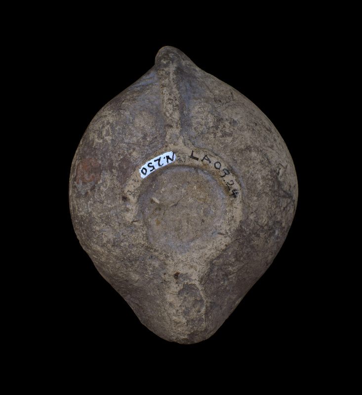 Round-carinated, convex biconical reservoir with small discus surrounded by raised band; horizontally pierced vertical loop handle, from center of back of which raised band runs to ring base within which faint traces of  lightly incised ?letters/mark; fairly short rounded nozzle.  Shoulder decorated with four concentric rows of close-set raised dots.  Originally coated w darkish paint.  Nozzle darkened.