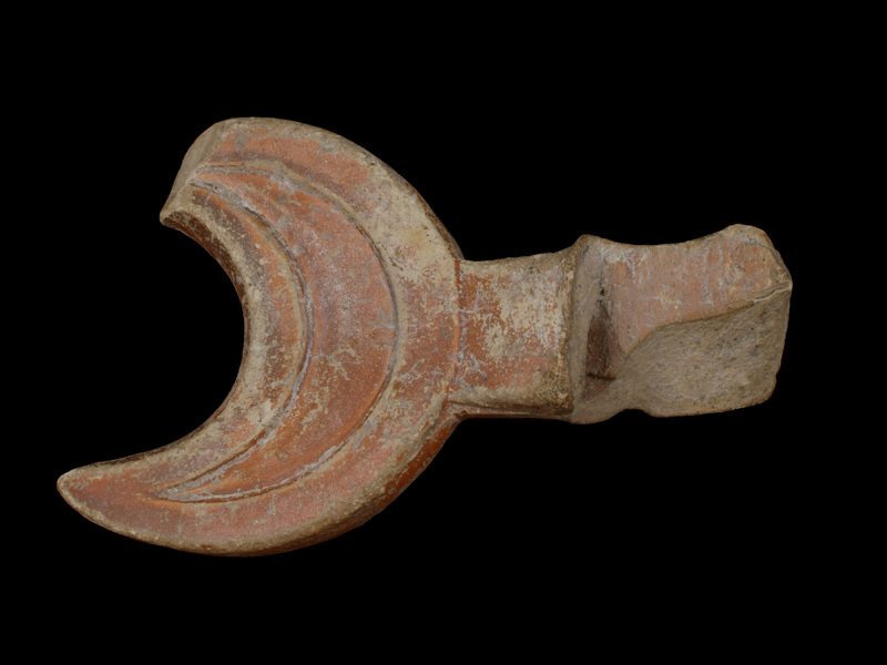 Crescent-shaped finial attached to horizontally perforated vertical loop handle.  Flat  exterior surface of finial recessed in center so as to produce broad raised edge.  Coated all over w reddish paint.