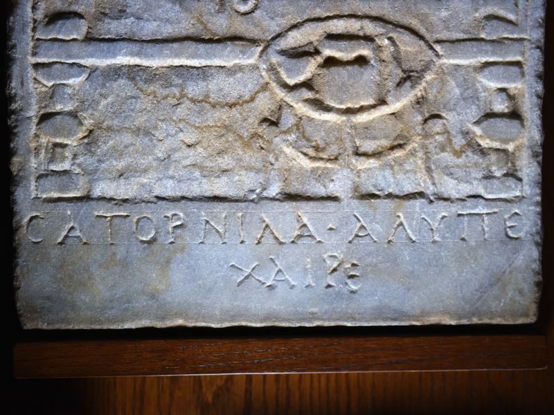 Rectangular stele w naiskos frame occupying 5/6 of surface, lower 1/6 given to inscription in large capitals:
 
ΣΑΤΟΡΝΙΛΑ • ΑΛΥΠΟ ΧΑΙΡΕ  
Satornila, daughter of Alypos, Greetings!

Within naiskos woman in chiton & himation reclining on kline w elaborately turned legs, in front of which round 3-legged table in birds-eye perspective on which large aryballos in center, smaller skyphos on l & ?dipper on r.  Woman reclines against triple-segmented pillow to her left, w upper body frontal, lower body profile; l arm bent, hand holding cup, r hand stretched out over lower body w handing holding ?purse;  features of face clearly articulated, hair in waves fr central part.