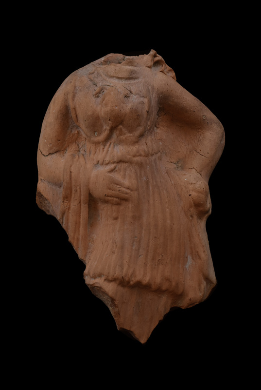 Mouldmade figure of  goddess standing w weight on l leg, r leg bent w bent r arm leaning on ?pillar; l arm bent at elbow & hand resting on hip.  Wearing peplos w overfold almost to knees belted under short kolpos; aegis represented by oval ridges around breasts w Medusa-head in center; articulation of Gorgon hairline and eyes.  Folds of ?himation  coming from rear over r arm and falling along r leg; vertical folds of peplos clearly articulated.  R hand flat on belly w fingers articulated; l left hand holds unidentified object against hip.  Large vent-hole in plain back.