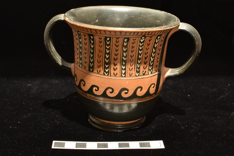 Kantharos of Saint-Valentine class.  On one face central panel of black on red and white on black feathered scales with side stripes of V's and horizontal band of leaves below, short vertical stripes above.  On other face central panel of alternating vertical stripes of black V’s on red and white V’s on black with single stripe at left of dots and hook band .below, vertical stripes above.  Interior handles and lower body solidly coated; reserve band above base which solidly coated inside and out; interior of base reserved except for circular band around center.