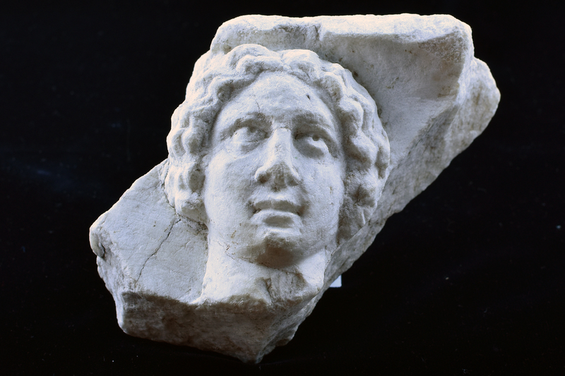 Fragment w head & neck of ?woman facing front w curly hair  waving from central part to jawline; eyes, nose and mouth articulated.  Flat top surface rough picked.