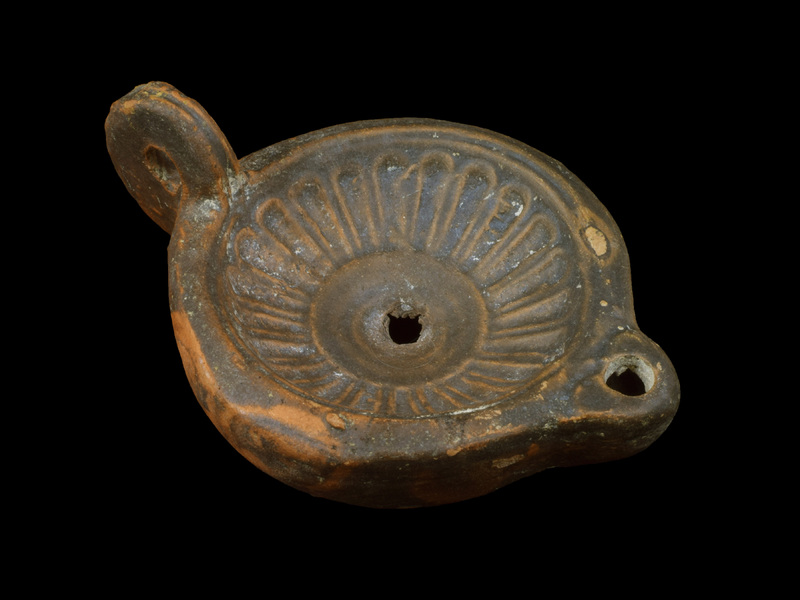 Convex-sided reservoir curving sharply to deeply concave discus which decorated with multi-petaled rosette with plain rim around crudely punched filling hole  near which shallow depression; shallowly concave base with 2 concentric incised lines defining edge and ? very lightly incised X V in center; short rounded nozzle and high swinging loop handle which has incised line down center toward discus but is crudely punched on back surface, incised lines making V at contact of handle with reservoir.  Completely coated with mottled dark paint.