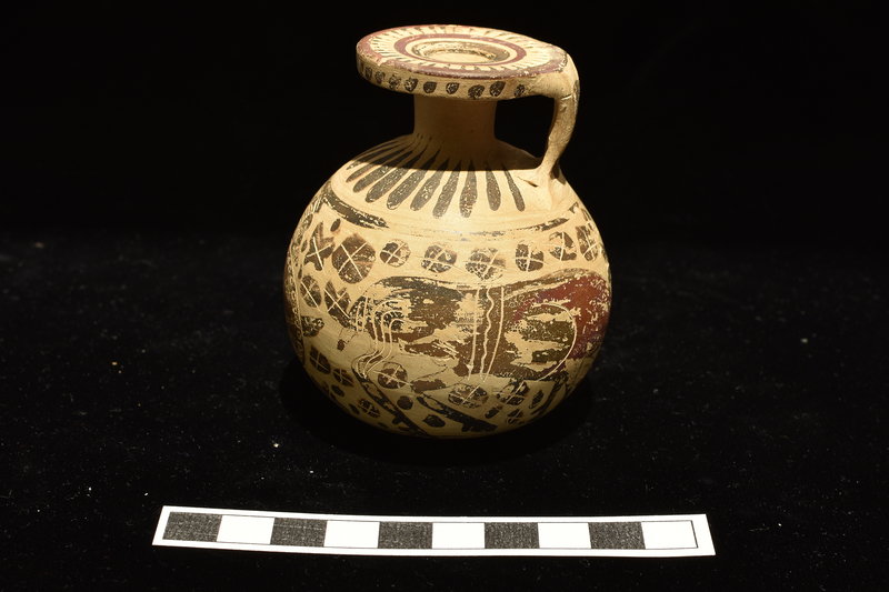 Small full-bodied aryballos.  Main decoration around body between two stripes: warrior opposite handle and two grazing deer around back and sides, blob rosettes in field; figures decorated with incision and added red, rosettes with incision only.  Base decorated with stripes radiating from central annulus.  Radiating elongated drops on shoulder; irregular dots on edge of rim, surface of rim decorated with 3 concentric stripes with elongated triangles radiating inward from exterior stripe; two broad stripes on exterior handle.
