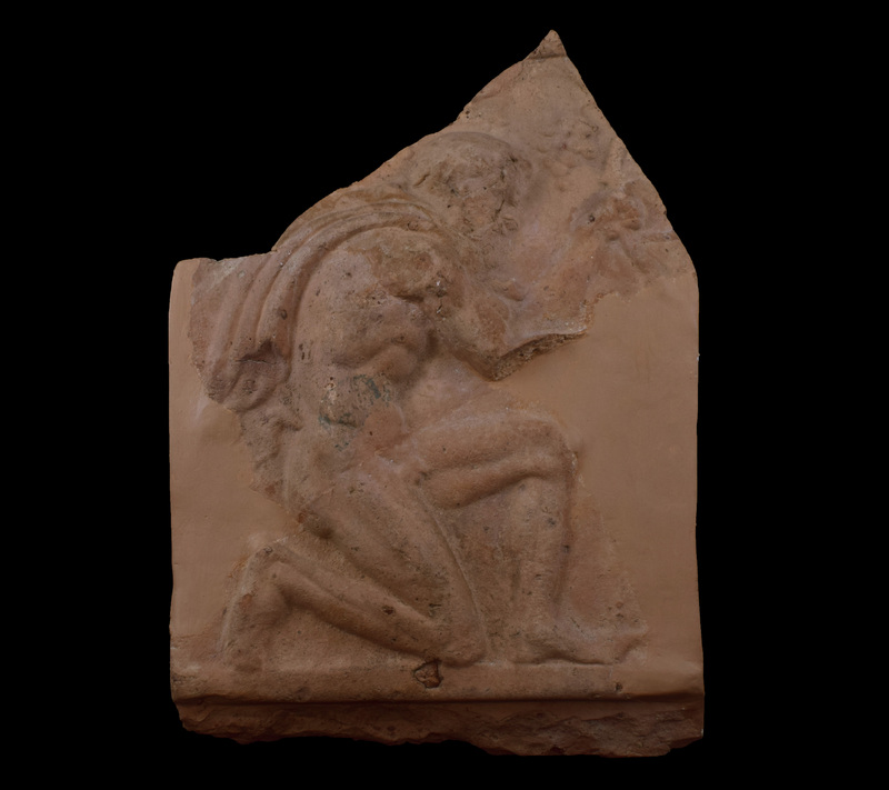 Relief figure of kneeling satyr facing right with left arm stretched up to grape vine and right arm less strongly bent; well muscled body in baroque style with cloak tied at neck and curving down back to just above small tail; bearded with full head of curly hair, articulation of eye by rounded depression, and open mouth.  In front of and above head of satyr bunches of grapes.  Figure rests on low raised border beneath which flat, apparently undecorated band extends to finished edge of plaque.  Patch of green paint on body, probably modern.