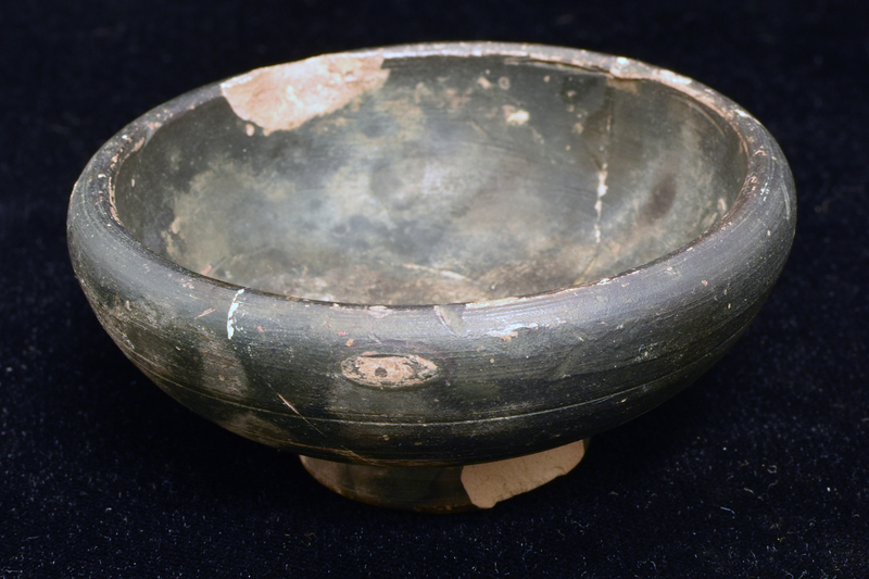 Bowl w full convex sides curving in just at thick rim, ring base with deeply concave underside w prominent central nipple.  Coated all over w dark paint except for part of ext & most of underside of base.