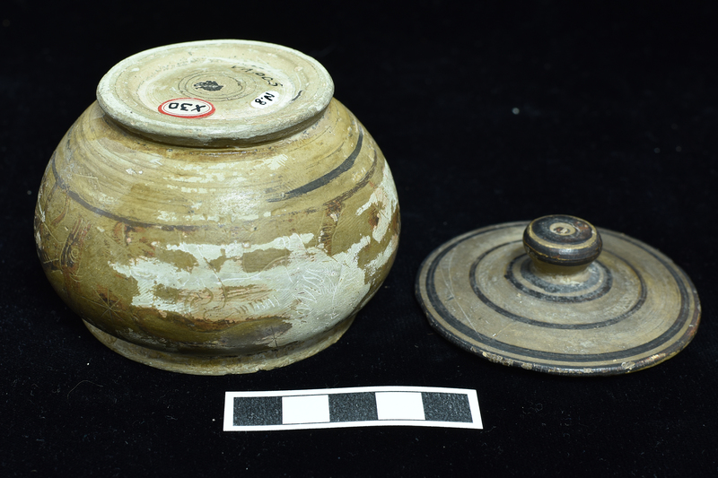 N.8a: Low convex-bodied pyxis w primary decoration on body  between narrow  stripes: heraldic sphinxes on either side of incised staff with two stars above , another below; at rear grazing deer and lion; blob rosettes in field;  figures and rosettes  decorated with incision; low flaring base decorated with dark stripe on bottom edge. N.8b: Lid, probably not belonging, fairly flat with conical handle, decorated with  narrow concentric stripes with top of handle solidly coated.
