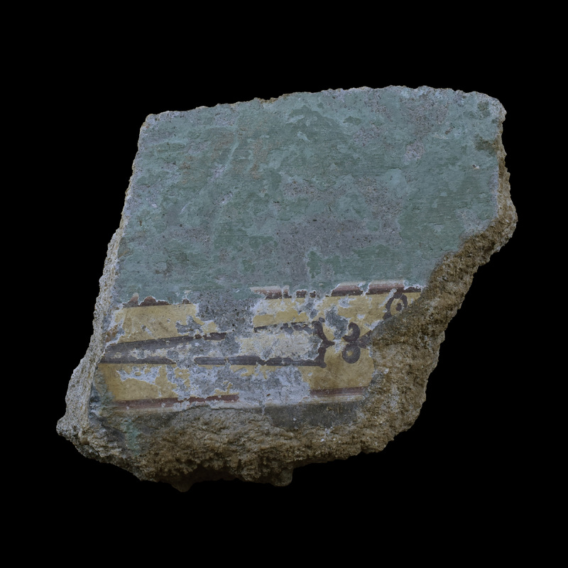Fairly thick fragment with flat surface where original back preserved.  Primary wall surface painted plain green; single decorative ?h/v  band pres: background  yellow with borders of narrow black red and white stripes with traces of solid black band or panel toward broken edge of one side; within band decoration in black, probably originally consisting of elongated, sword-like elements separated by lozenge-shaped elements terminating in opposing loops.