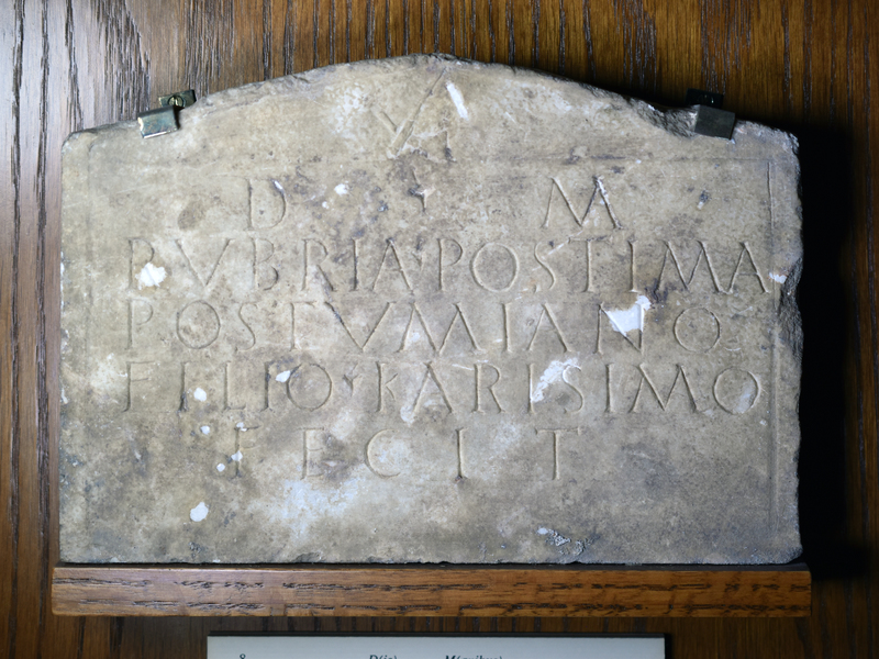 Plain plaque of white marble with border; in the pediment, a small stone-mason's dolabra, pick.
